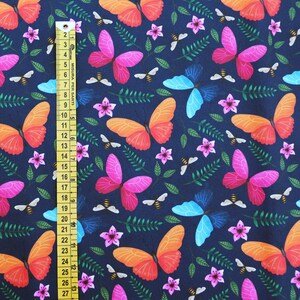 May include: A dark blue fabric with a repeating pattern of butterflies, flowers, and bees. The butterflies are in shades of pink, orange, and blue. The flowers are pink and white. The bees are yellow.