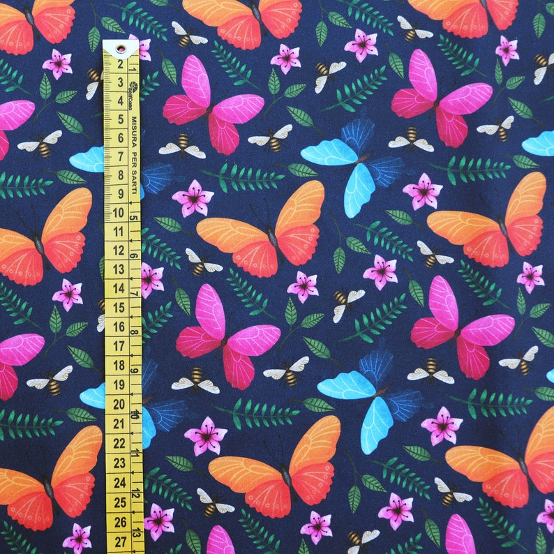 May include: A dark blue fabric with a repeating pattern of butterflies, flowers, and bees. The butterflies are in shades of pink, orange, and blue. The flowers are pink and white. The bees are yellow.