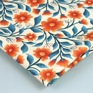Puede incluir: Una tela de color crema con un patrón repetitivo de flores naranjas y hojas verde azuladas. La tela está doblada por la mitad y el patrón es visible en ambos lados.