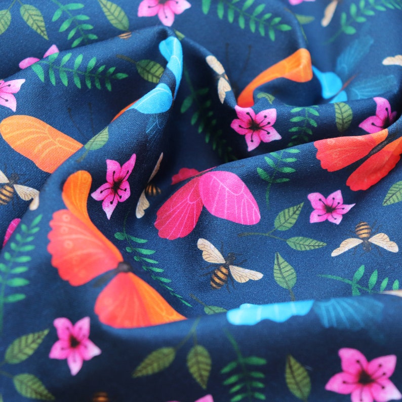 May include: A navy blue fabric with a repeating pattern of butterflies, flowers, and bees. The butterflies are in shades of pink, orange, and blue. The flowers are pink and white. The bees are yellow and brown.
