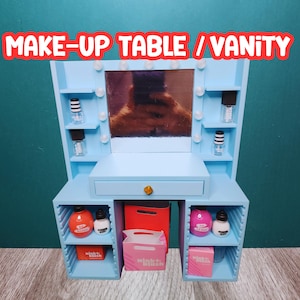 May include: A light blue vanity table with a mirror and a drawer. The mirror has a row of lights around it. The table has two shelves on each side. The shelves are filled with various bottles and containers. The text "MAKE-UP TABLE / VANITY" is written in white letters on a blue background at the top of the image.