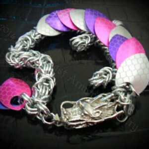 May include: A silver chainmail bracelet with a dragon head charm. The bracelet is decorated with pink, purple, and white scales.