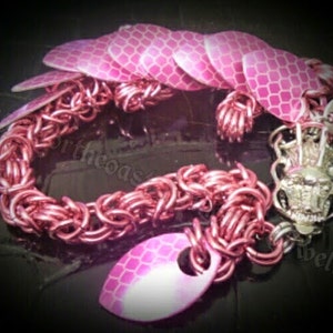 May include: A pink and silver bracelet with a dragon scale design. The bracelet is made of metal and has a chain link pattern. The scales are made of a reflective material.