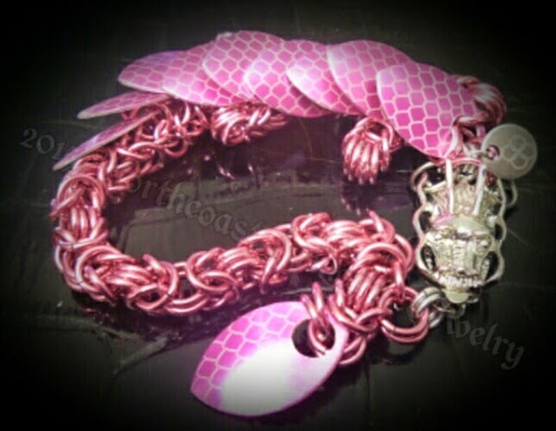 May include: A pink and silver bracelet with a dragon scale design. The bracelet is made of metal and has a chain link pattern. The scales are made of a reflective material.