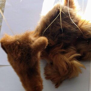 May include: A brown plush toy dog with long fur, hanging from strings. The dog is lying on its back with its legs in the air.