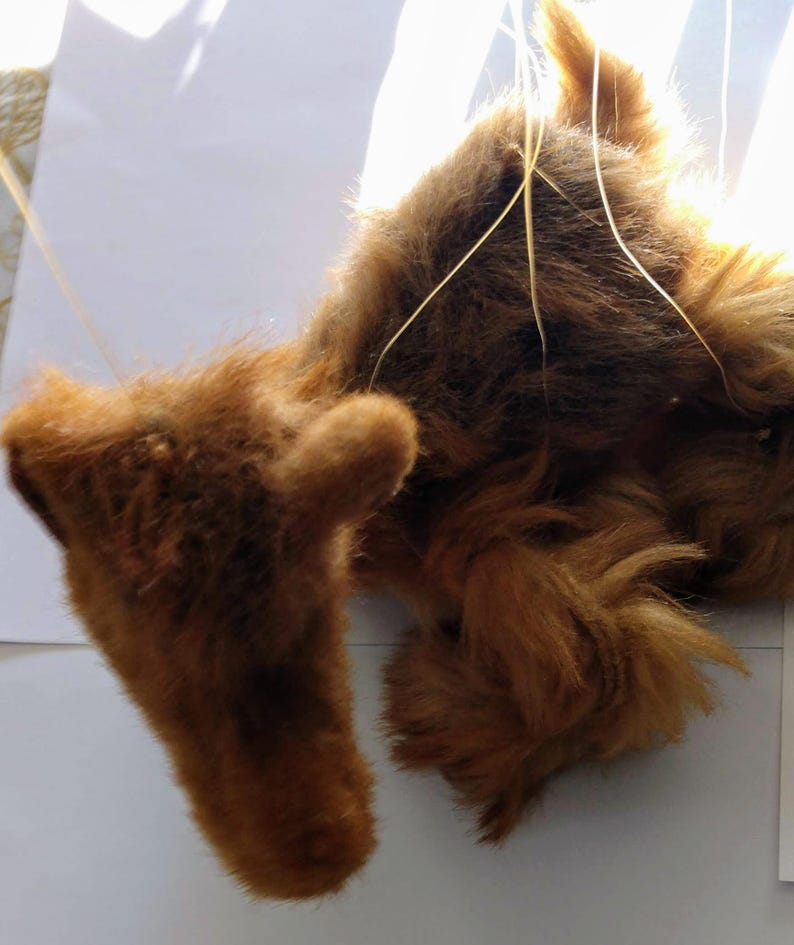 May include: A brown plush toy dog with long fur, hanging from strings. The dog is lying on its back with its legs in the air.