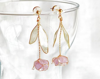 Può includere: Un paio di delicati orecchini dorati con accenti di fiori rosa e dettagli di foglie bianche. Gli orecchini sono pendenti e presentano un design delicato in filo.