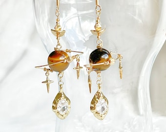 May include: Gold dangle earrings with a tiger's eye stone, a crystal, and gold accents.