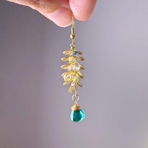 May include: A gold-colored earring featuring a cascading design with small, colorful beads and a teardrop-shaped, teal-colored gemstone at the bottom. The earring has a delicate, floral-inspired structure, with a hook for easy wear.