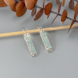 May include: Silver dangle earrings with a hammered rectangular pendant and blue gemstone accents.