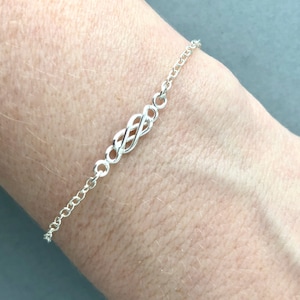 May include: A silver chain bracelet with a Celtic knot design. The bracelet is on a person's wrist.
