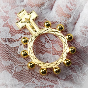 以下が含まれることがあります： 金色のロザリオリング。十字架と円形のデザイン。十字架にはイエスの描写と「INRI」の碑文があります。リングには10個の金色のビーズが付いています。ロザリオリングは宗教的なアイテムです。