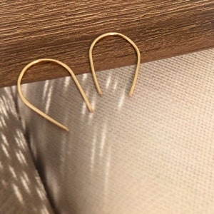 May include: A pair of gold-toned hoop earrings with a simple, minimalist design. The earrings are made of a thin, curved wire that forms a U-shape.