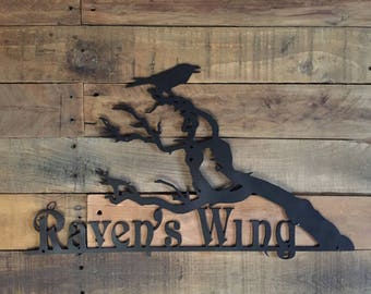 May include: Black metal wall art featuring a raven perched on a branch with the text "Raven's Wing" below.