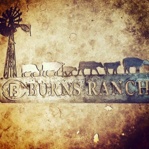 May include: A metal sign with the words "Burns Ranch" in a stylised font. The sign features a silhouette of a windmill and a line of cattle walking across a field.