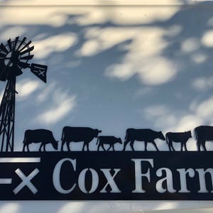 May include: Black metal silhouette of a windmill with a sign that reads "Cox Farm" and a line of cows walking below.