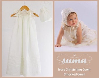 Puede incluir: Vestido de bautizo de color marfil con smocks. El vestido está hecho de una tela suave y ligera y presenta un diseño simple y elegante. El vestido se muestra en una niña pequeña que lleva una capota a juego.