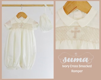 Pode incluir: Macacão branco de algodão com smock e detalhe de bordado de cruz. O macacão tem um colarinho Peter Pan e é feito de um tecido macio e leve. Vem com um gorro a condizer.