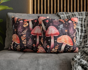 May include: Two rectangular throw cushions featuring a dark background with a watercolour design of red and white mushrooms, ferns, and foliage. The cushions rest on a grey sofa.