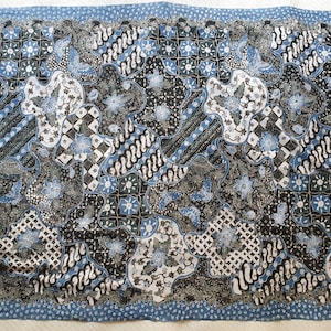 Könnte beinhalten: Ein gemusterter Stoff mit einem sich wiederholenden Design in Blau, Schwarz und Weiß. Das Muster umfasst Blumen- und Schmetterlingsmotive mit geometrischen Formen und stilisierten Linien. Der Stoff hat einen Rand mit kleinen blauen Punkten.