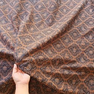May include: Brown and black patterned fabric with a repeating geometric design. The fabric has a detailed, ornate pattern with floral and leaf-like motifs. The fabric is draped, showing the texture and flow of the material.