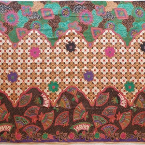 Könnte beinhalten: Ein farbenfrohes Textil mit einem sich wiederholenden Muster. Das Design zeigt geometrische Formen, florale Motive und fächerartige Elemente in Braun-, Grün-, Rosa- und Lilatönen. Der Stoff hat einen dekorativen Rand.