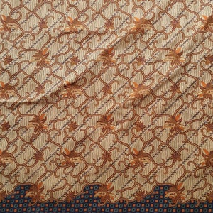 Op de afbeelding: Een beige stof met een herhaald patroon van bruine bloemen en wijnstokachtige ontwerpen. De stof heeft een donkerblauwe rand met een herhaald vierkant patroon. Het algehele ontwerp is ingewikkeld en gedetailleerd, met een vintage esthetiek.