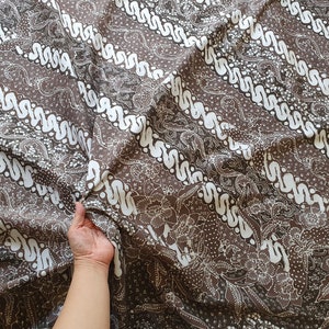 Könnte beinhalten: Brauner Stoff mit einem weißen, sich wiederholenden Wellenmuster und floralen Designs. Der Stoff ist gefaltet, wodurch seine Textur und sein Muster sichtbar werden. Geeignet für Kleidung oder Heimdekoration.