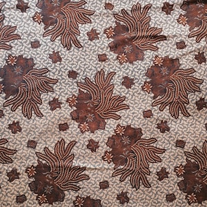 Może przedstawiać: Tkanina z powtarzającym się wzorem dużych, stylizowanych brązowych wzorów kwiatowych o skomplikowanych detalach. Tło jest w jasnym odcieniu beżu z małym, powtarzającym się wzorem. Całkowity projekt jest symetryczny i szczegółowy.