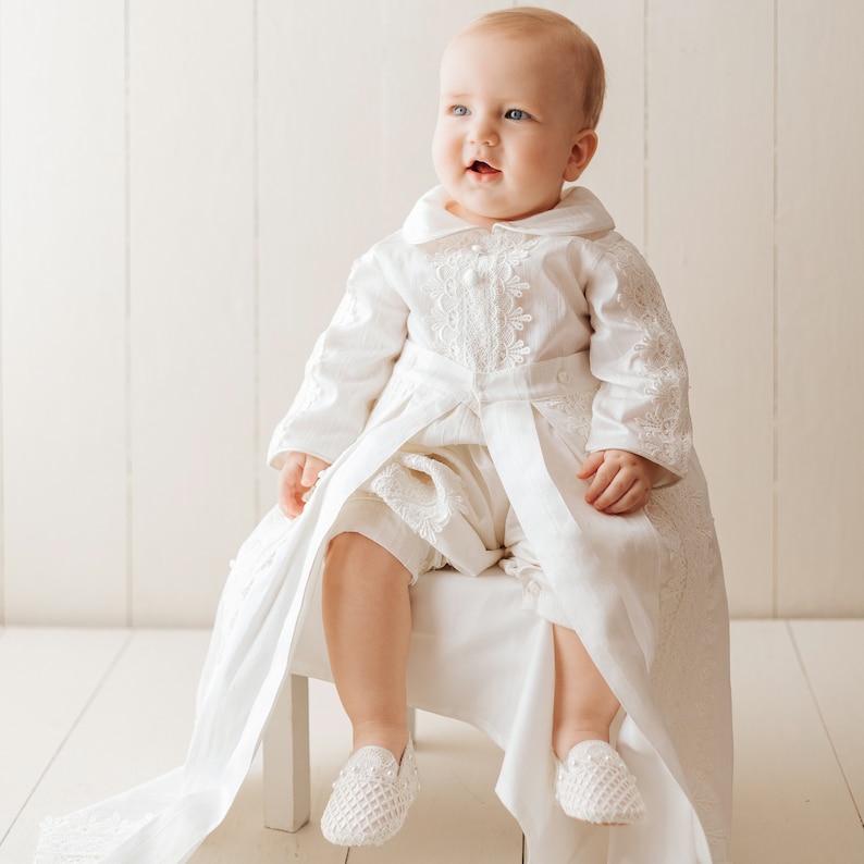 Adorable baby smiling and wearing our removable ivory long-sleeved boy's christening robe, with fine embroidered details, with high-quality fabric to provide comfort to the baby
