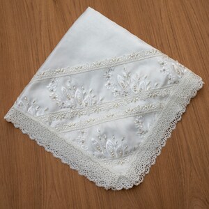 May include: White satin fabric with a delicate lace trim and embroidered floral design. The embroidery features small white beads.