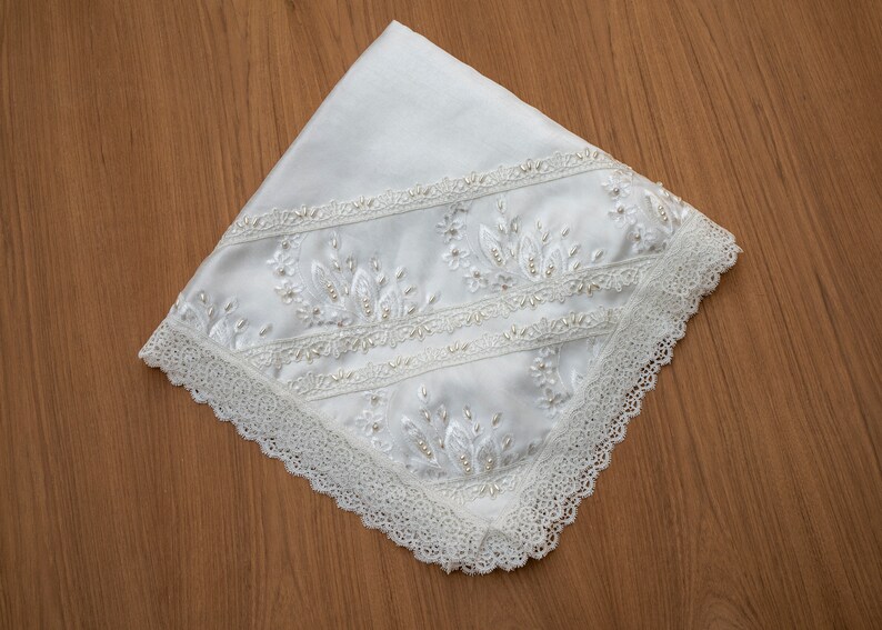 May include: White satin fabric with a delicate lace trim and embroidered floral design. The embroidery features small white beads.