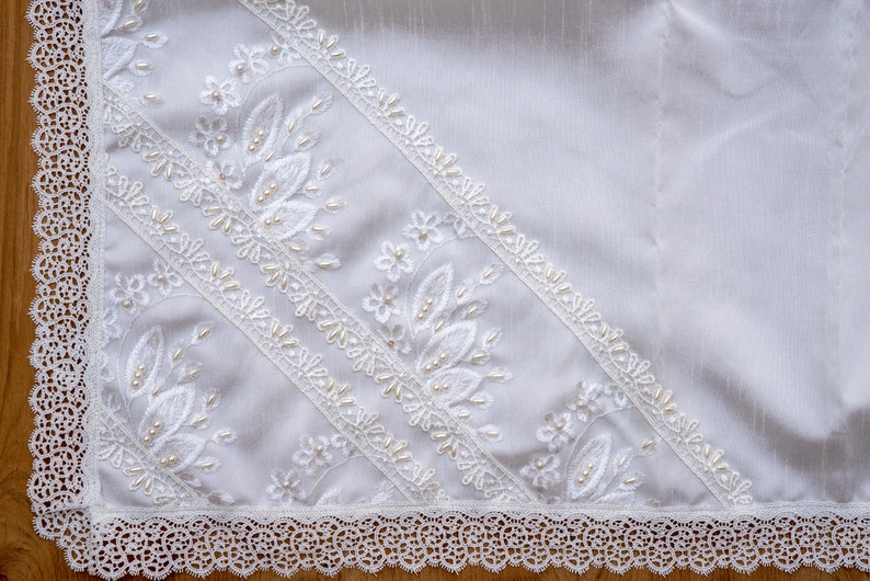 May include: White lace fabric with delicate floral embroidery and pearl accents. The fabric has a scalloped edge and is ideal for crafting or decorating.
