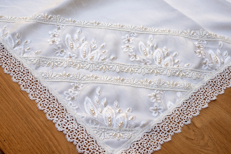 May include: White table runner with delicate lace trim and pearl embellishments. The lace is a delicate pattern with a scalloped edge. The runner is perfect for a wedding or special occasion.