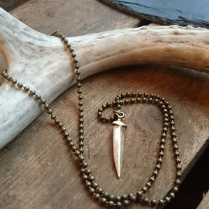 May include: A silver dagger pendant on a brown beaded chain. The chain is draped over a white antler.