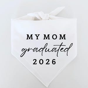 Puede incluir: Bandana blanca con el texto "MY MOM graduated 2026" en negro. La bandana está anudada en la parte superior. El texto es una mezcla de una fuente en negrita sin serifa y una fuente cursiva.