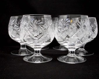 May include: Set of six clear crystal glasses with intricate cut designs. The glasses have a wide bowl and a short stem.