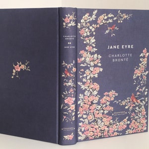 Puede incluir: Un libro de tapa dura de color azul marino con un diseño floral en la portada. El título "Jane Eyre" y el autor "Charlotte Bronte" están impresos en blanco en la portada. El libro es de Cranford Editions.