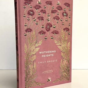 Pu&ograve; includere: Un libro con copertina rigida intitolato Wuthering Heights di Emily Bront&euml; della Cranford Collection. La copertina &egrave; di colore rosa polvere con illustrazioni dorate di alti papaveri, steli e piccole api sulla parte anteriore.