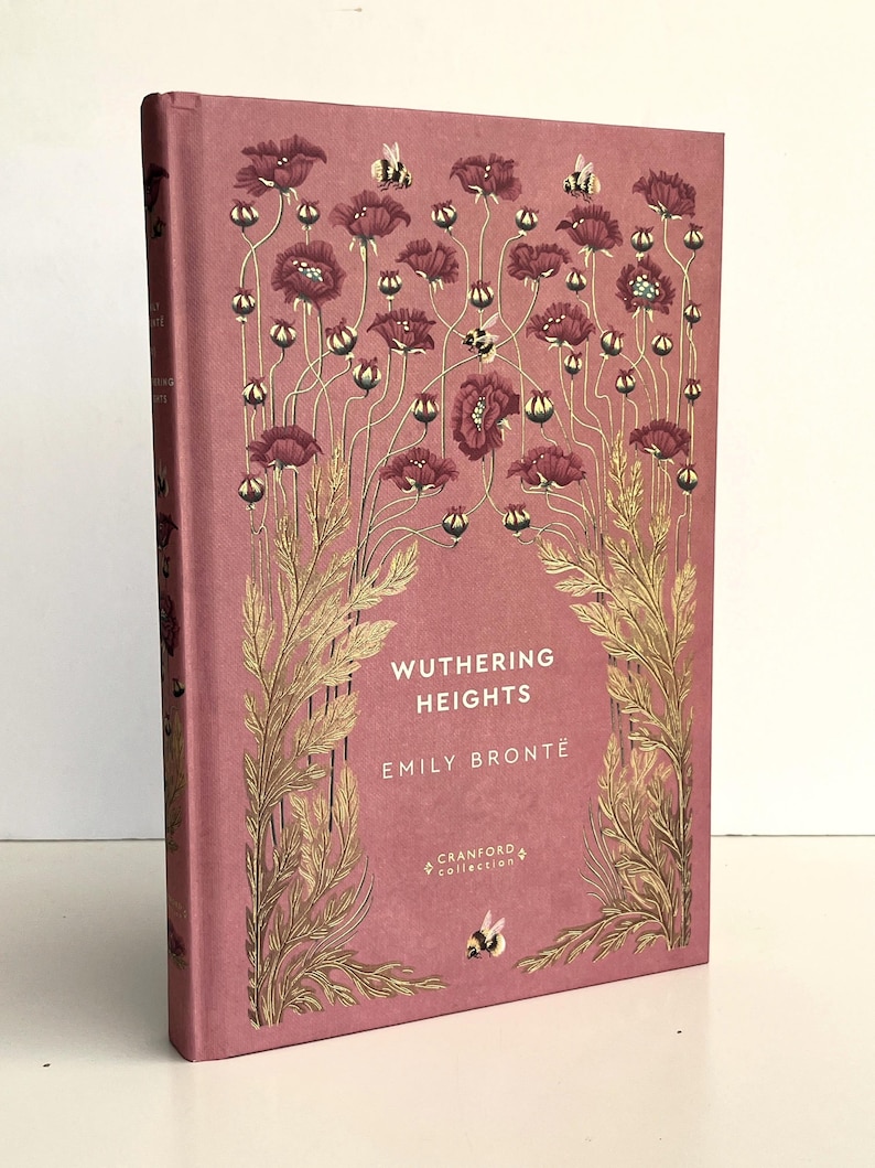 Pu&ograve; includere: Un libro con copertina rigida intitolato Wuthering Heights di Emily Bront&euml; della Cranford Collection. La copertina &egrave; di colore rosa polvere con illustrazioni dorate di alti papaveri, steli e piccole api sulla parte anteriore.