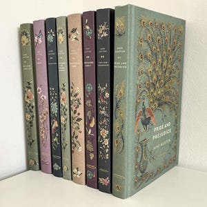 Puede incluir: Una colección de libros de Jane Austen con diseños florales y de pavo real. Las portadas muestran títulos como "Orgullo y Prejuicio" y "Mansfield Park". Los libros son de varios colores, incluyendo verde, morado y beige.