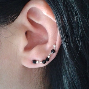 May include: A silver ear cuff with black beads. The cuff is curved and has five black beads.