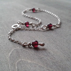 Garnet bracelet against a wooden background. Garnet beads are added at even intervals through the chain that forms this bracelet. One of the links of the chain is used to close the bracelet.