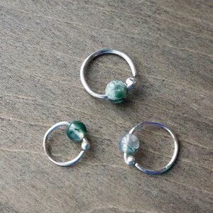 Three sterling silver hoops with bead of moss agate on wooden background. This hoop is offered with moss agate  in a variety of colors and textures