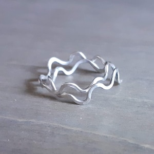 May include: A silver ring with a wavy design. The ring is made of two layers of metal, creating a double wave effect.