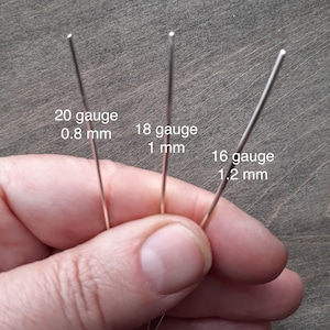 Sterling silver wire in three different gauges held by a hand. The thinnest, 20 gauge is 0.8 mm. The medium one, 18 gauge is 1 mm. The thickest, 16 gauge is 1.2 mm.