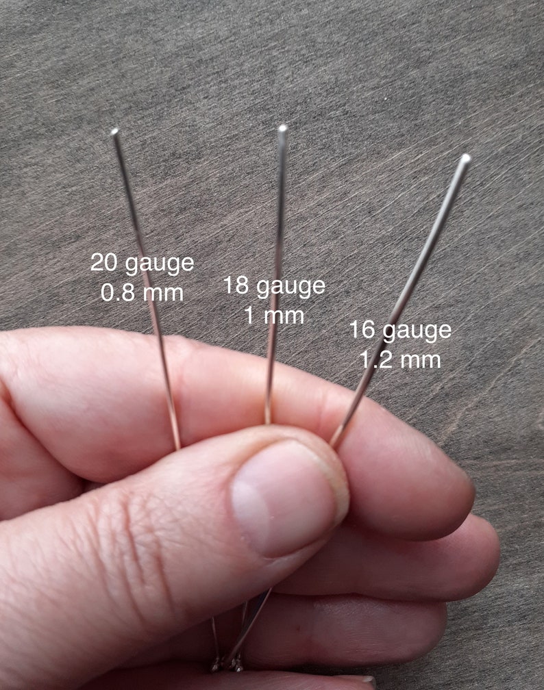 Sterling silver wire in three different gauges held by a hand. The thinnest, 20 gauge is 0.8 mm. The medium one, 18 gauge is 1 mm. The thickest, 16 gauge is 1.2 mm.