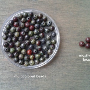 Dragons blood s beads against a wooden background. The beads display a variety of colors, from red, white and yellow to medium and dark green. Some beads are almost exclusively in dark green.