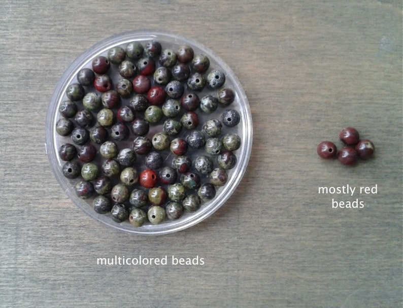 Dragons blood s beads against a wooden background. The beads display a variety of colors, from red, white and yellow to medium and dark green. Some beads are almost exclusively in dark green.