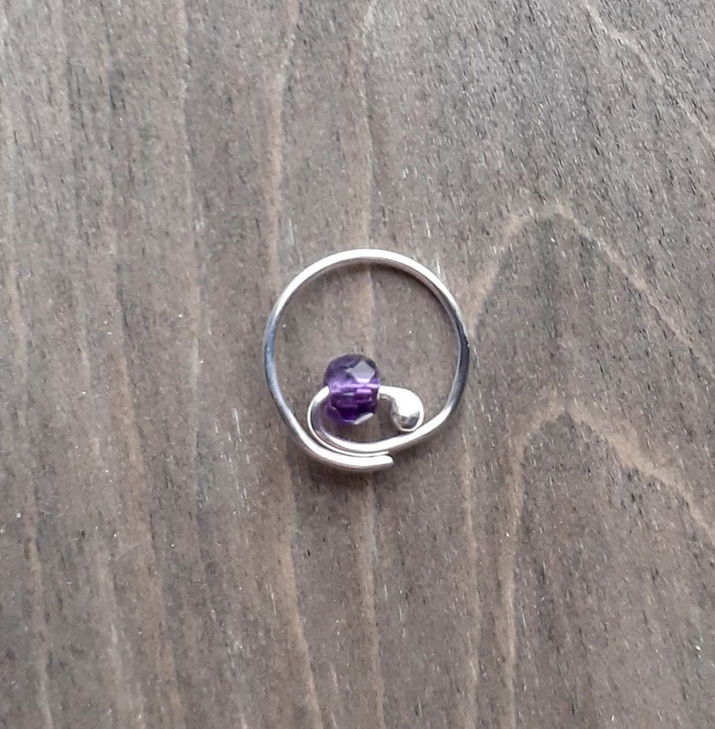 Earring with amethyst bead on a wooden background.